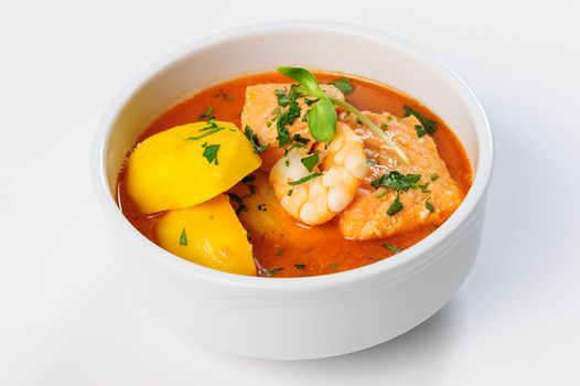 A bowl of fish soup with salmon, shrimps and potato at natural white background