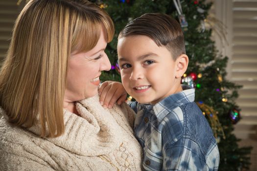 Happy Mother and Mixed Race Son Hug Near Their Christmas Tree.