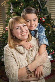 Happy Mother and Mixed Race Son Hug Near Their Christmas Tree.