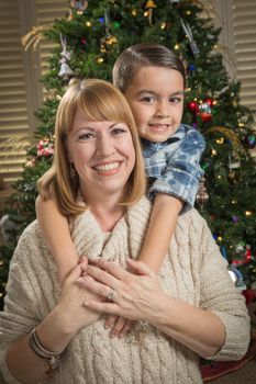 Happy Mother and Mixed Race Son Hug Near Their Christmas Tree.