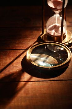 Vintage hourglass near magnifying glass on wooden background with long shadow