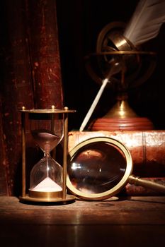 Vintage still life. Magnifying glass near hourglass on background with old book