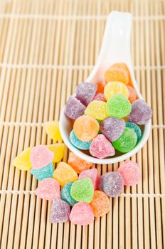 Colorful candies, jelly sugar in white spoon on bamboo mat.