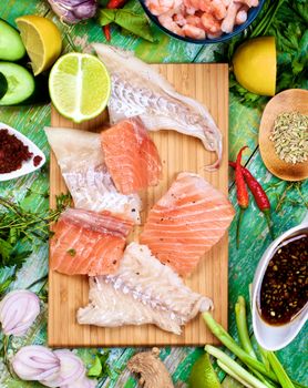 Arrangement of Raw Ingredients of Thai Fish Cakes with Vegetables, Spices, Herbs, Fruits, Prawns and Delicious Fillet of Salmon and Cod closeup on Cracked Wooden background