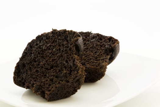 Rich and moist chocolate muffin sliced in half on white plate. Delicious, sweet food background. 