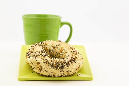 Bagel and coffee presentation with garlic, sesame and poppy seeds as topping and green mug adjacent.  Still life in horizontal image with copy space. Crumbs on plate. 