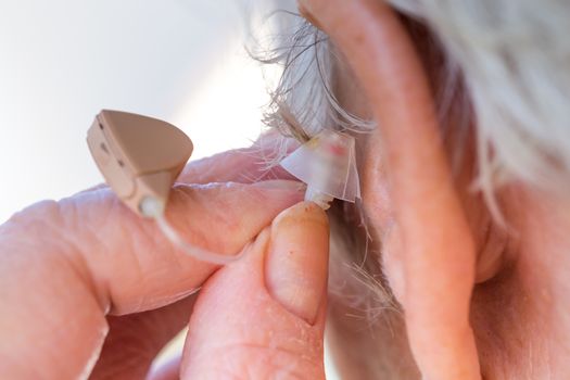 closeup senior woman inserting hearing aid in her ears