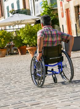 Back view of a disabled man rolling down the street in his wheelchair