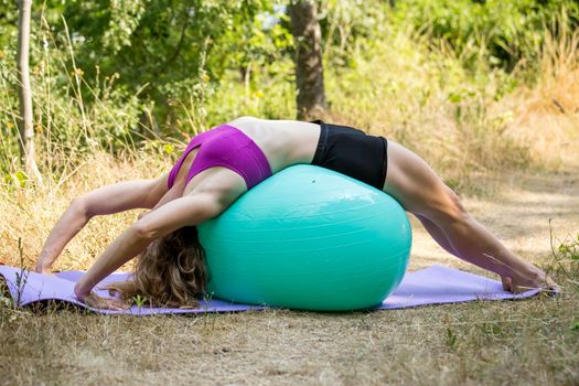 A woman performing a belly-buster on an exercise ball out in the woods