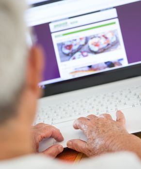 Closeup on pair of old hands typing on a laptop ontop of a desk.