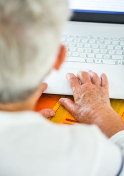 Closeup on pair of old hands typing on a laptop ontop of a desk.