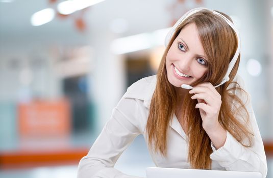 Beautiful young customer service representative using headset in office