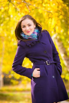 Self-confident girl in a dark blue coat against the background of autumn leaves