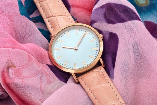 Classic pink wrist watch on colourful silk fabric background