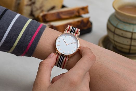 Girl's hand with wrist watches at the coffee break in front of hot chocolate and cake