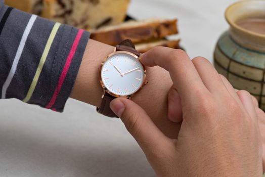 Classic wrist watch on girl's hand in front of hot chocolate and cake