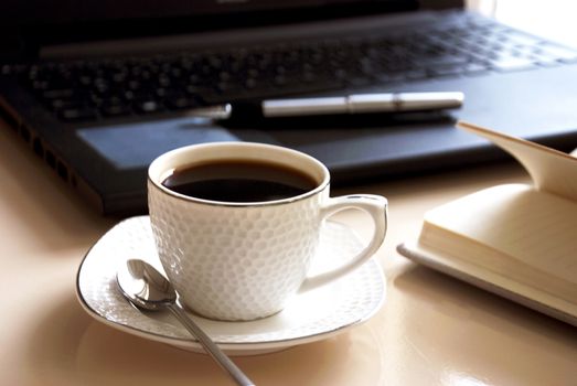 Work office desk with a cup of coffee computer laptop, notebook, pen.