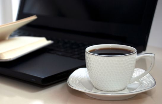 Work office desk with a cup of coffee computer laptop, notebook, pen.