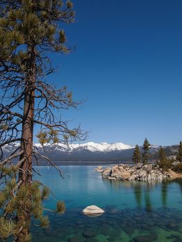 Scenic view of beautiful Lake Tahoe in Spring, landscape of the United States of America, clear water, nice sky, stone island, tree, fresh air and snow mountains