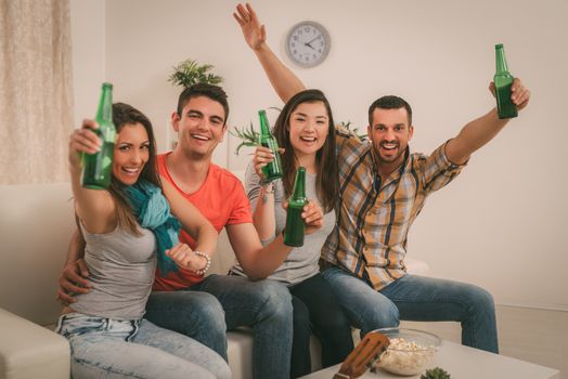 Friends enjoying with beer and cheers together at home party. Looking at camera.