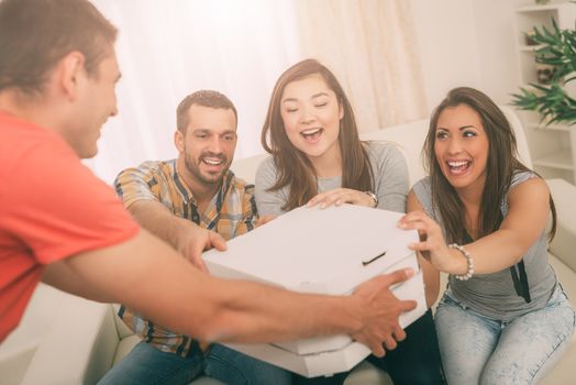 Four cheerful friends enjoying pizza together at home party. Selective focus.