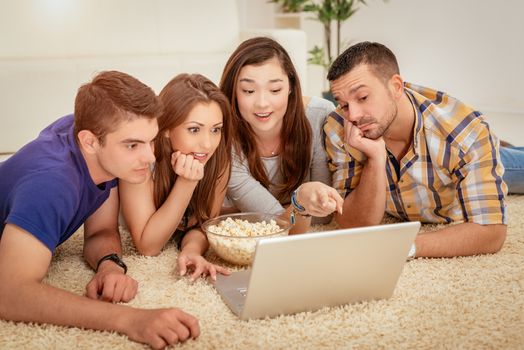 Four cheerful best friends having nice time in an apartment. They are watching movie together.