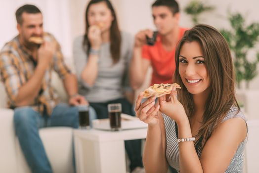 Close up of a young girl smiling and eating pizza. Her friends in the background. Selective focus. Focus on girl, on foreground.