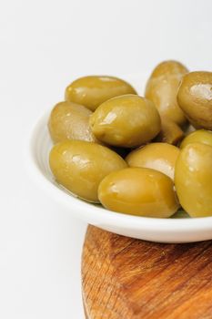 green olives in small white dish at wooden board