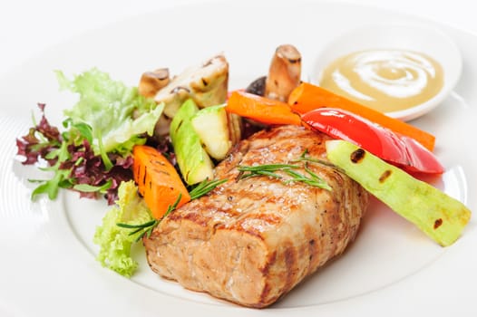 Grilled pork meat and vegetables on white plate with mustard sauce