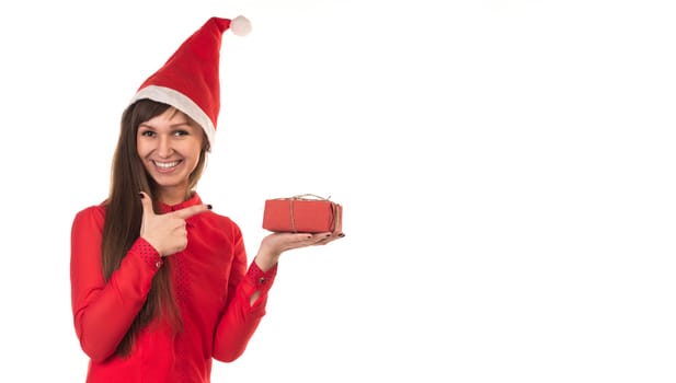 Young long-haired woman in red christmas cap points with her finger to red gift box