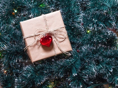 Christmas gift box on a fur-tree and garland background. Packaging holiday gifts