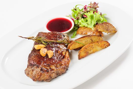 Thick juicy beef steak with berry sauce, lettuce, rosemary, nuts and fried potato, served on white plate