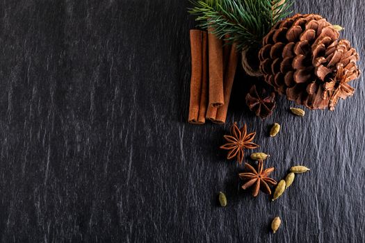 Cinnamon sticks, anise, cardamom and pine cone on a stone plate