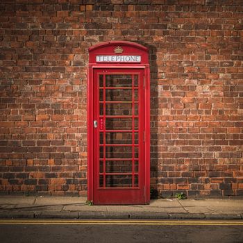 Grungy Traditional Red British Telephone Box Against A Red Brick Wall