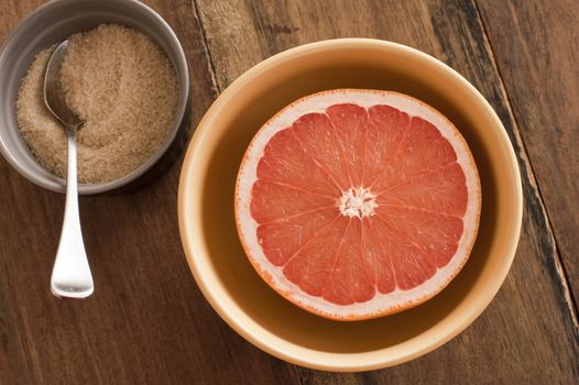 Fresh halved pink grapefruit served with an accompanying bowl of sugar for a healthy breakfast rich in Vitamin C