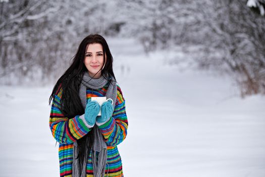 Beautiful young woman in a sweater. Winter outdoors walk with a cup of coffee