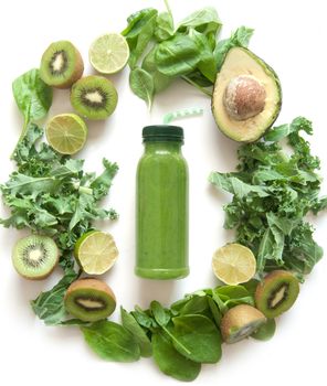 Bottled green smoothie surrounded with fruits and vegetables including spinach kale and avocado