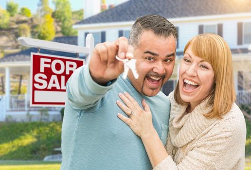 Happy Mixed Race Couple With Keys in Front of For Sale Real Estate Sign and New House.