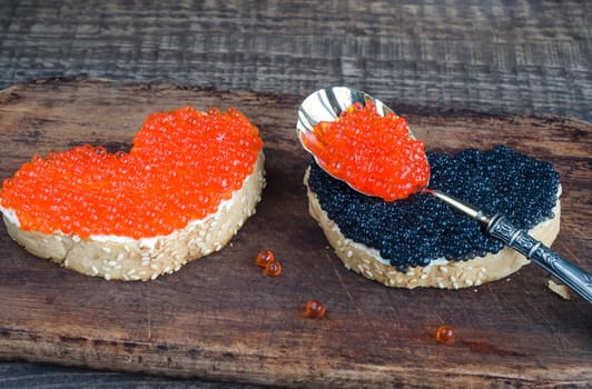 Sandwiches black and red caviar in the form of heart on a cutting Board and wooden background. Analog products.
