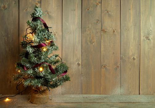 Christmas tree with lights against a wooden wall with space