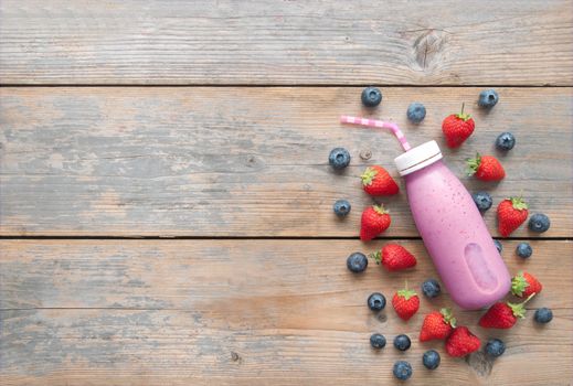 Berry smoothie bottle on top of a wooden background with space 