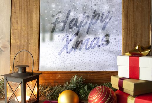 Xmas gifts decorations and a lantern next to a frosted window with hand written greeting