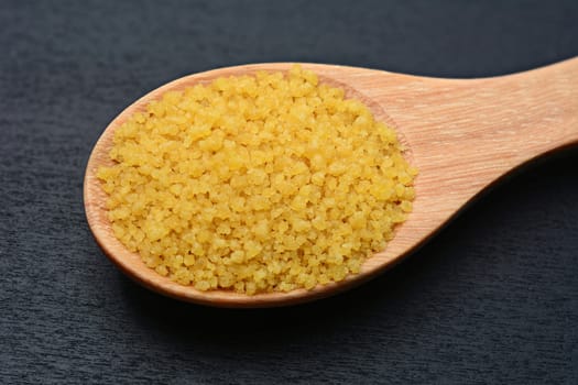 Brown sugar in wooden spoon and on black wooden table