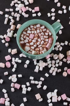 Hot chocolate in a green cup with marshmallows scattered around. Black background