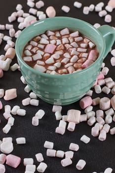 Hot chocolate in a green cup with marshmallows scattered around. Black background