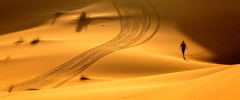 Merzouga, Morocco - Feb 24, 2016: Woman trekking along hot desert, beautiful orange sandy dunes, exploring Sahara, active vacation, discovering nature concept