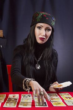 Sorceress wonders by Tarot cards on a black background