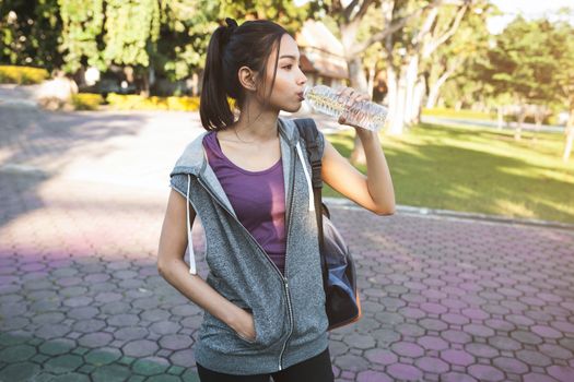 Portrait of young beautiful dark-haired woman in sport wearing drinking water at summer green park.