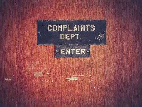 Retro Filtered Image Of A Grungy Complaints Department Sign On A Door