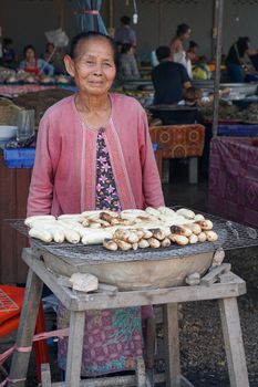 VIENTIANE, LAOS - FEBRUARY 19, 2016:  Old woman selling grilled bananas on a market on February 19, 2016 in Vientiane, Laos, Asia